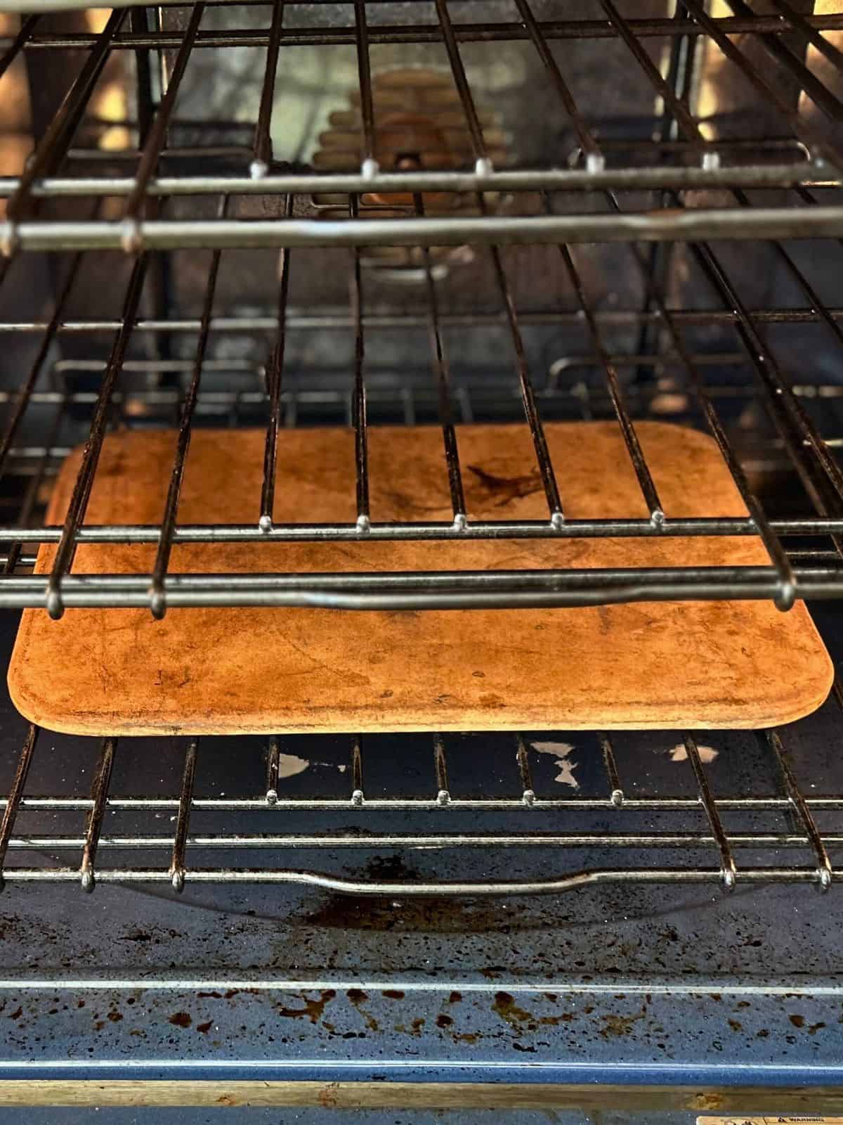 Rectangular pizza stone resting on a rack Inside an oven on the lowest rack position.