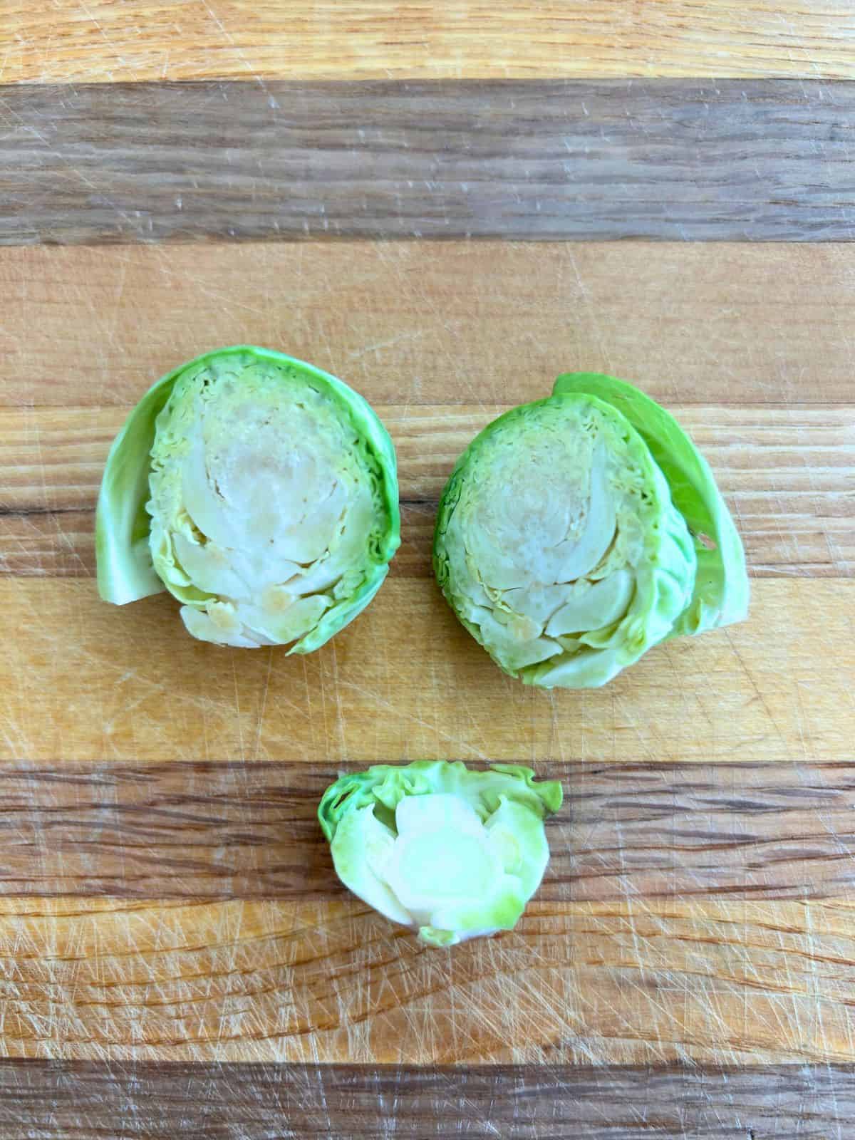 A single brussel sprout with the bottom core cut off and then remaining sprout is cut in half, flat sides facing up.