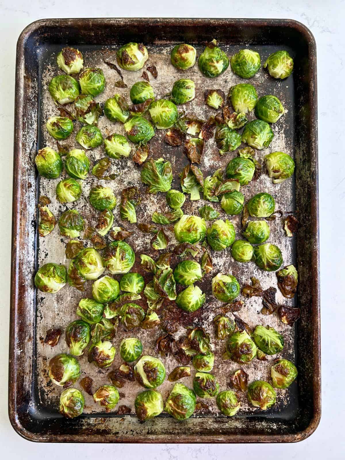 Finished oven roasted brussel sprout halves and leaves on a sheet pan after being in the oven.