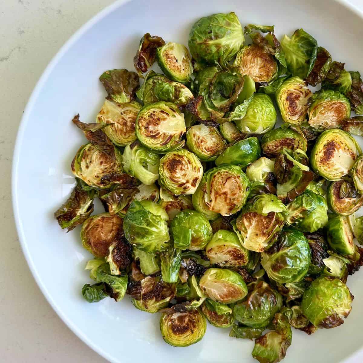 White coupe serving bowl with finished oven roasted brussels sprouts in a large pile ready for dinner.