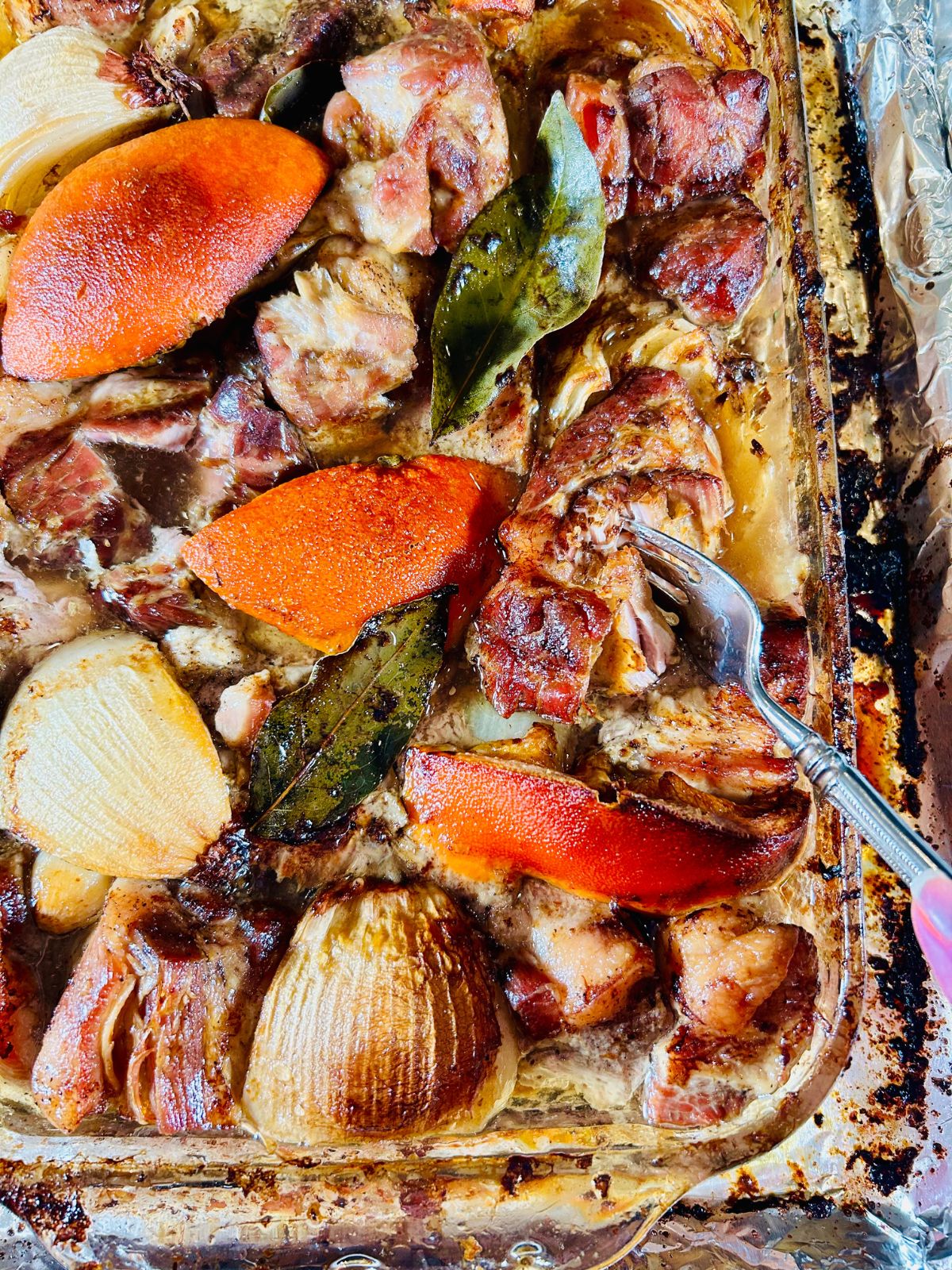 Cooked pork chunks, orange segment, and onions in a pyrex casserole with a fork poking thru a piece of pork.