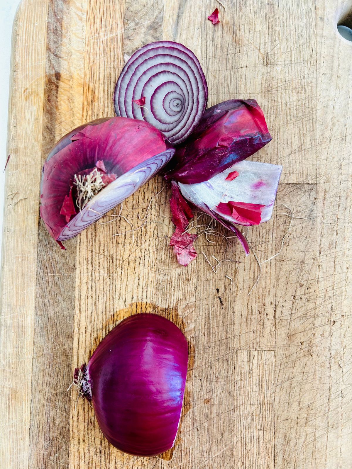 One half of a red onion peeled and ready to slice on the cutting board next to other half of the onion that has not been peeled.