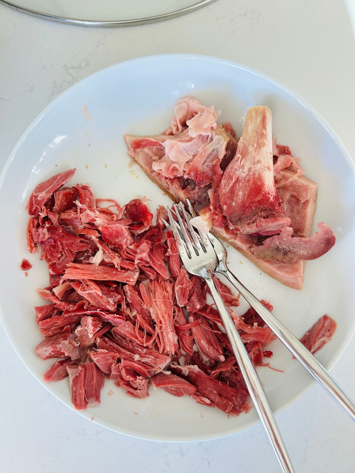 A white plate with shredded ham shank and two forks.