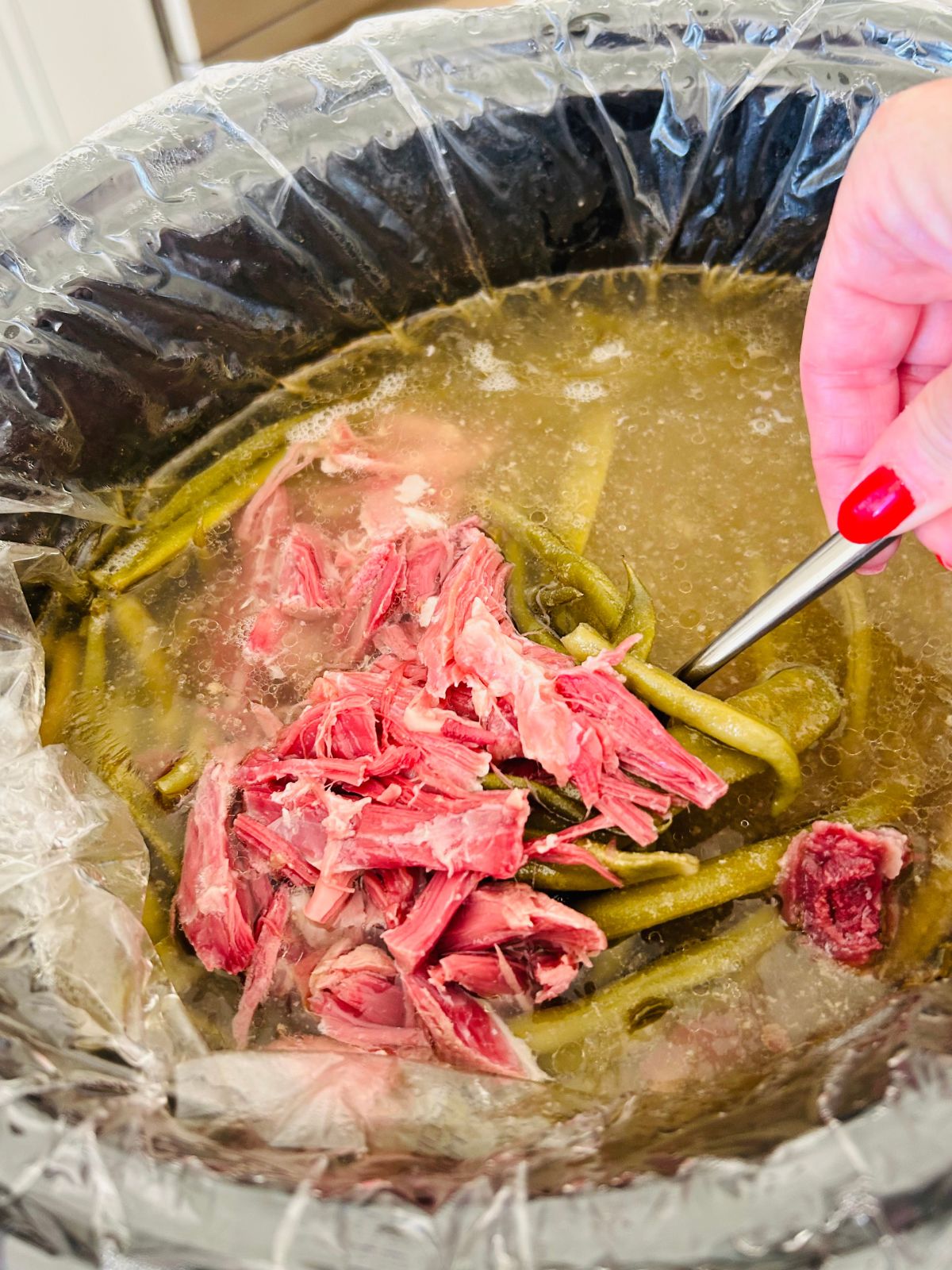 Shredded bite size pieces of pink ham from the ham shank returned back to the slow cooker of cooked green beans and broth.