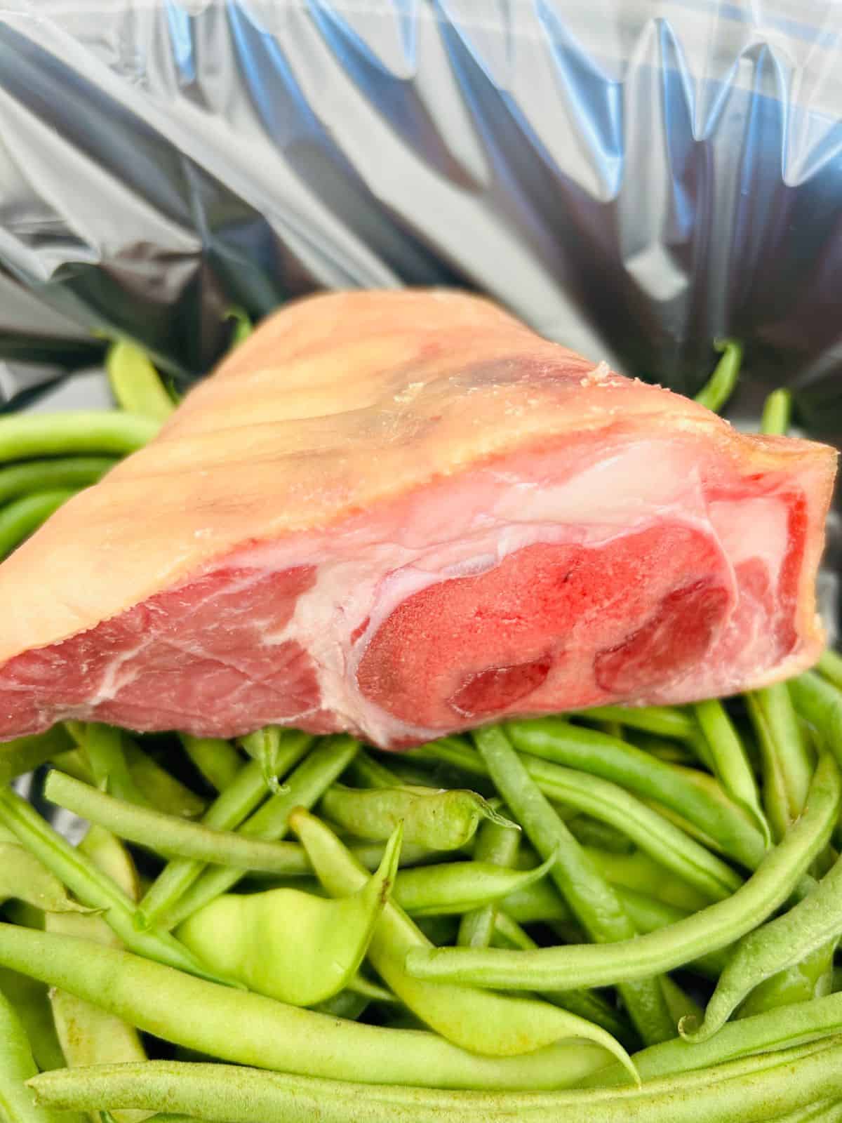 Close up side view of a cut ham shank showing the oozy collagen within the bone resting on top of green beans from the garden.