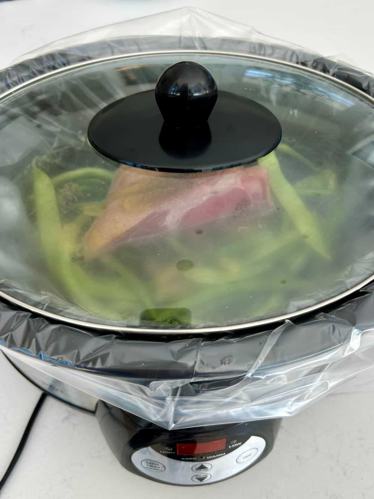 Slow cooker with steamy lid on and time set getting ready to cook the fresh green beans and ham shank.