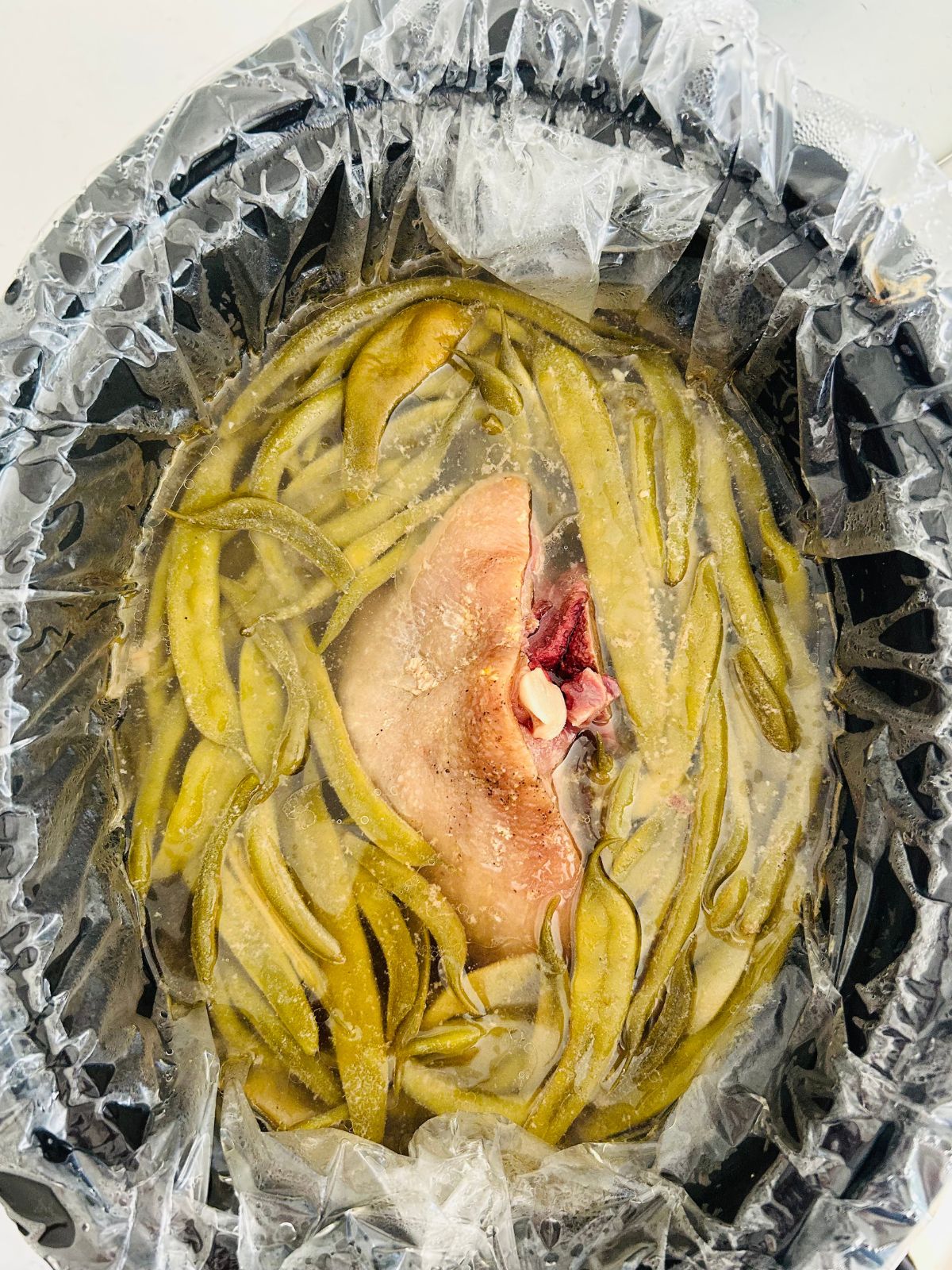 Simmered green beans and ham hock in the center of a slow cooker with a liner and no lid.