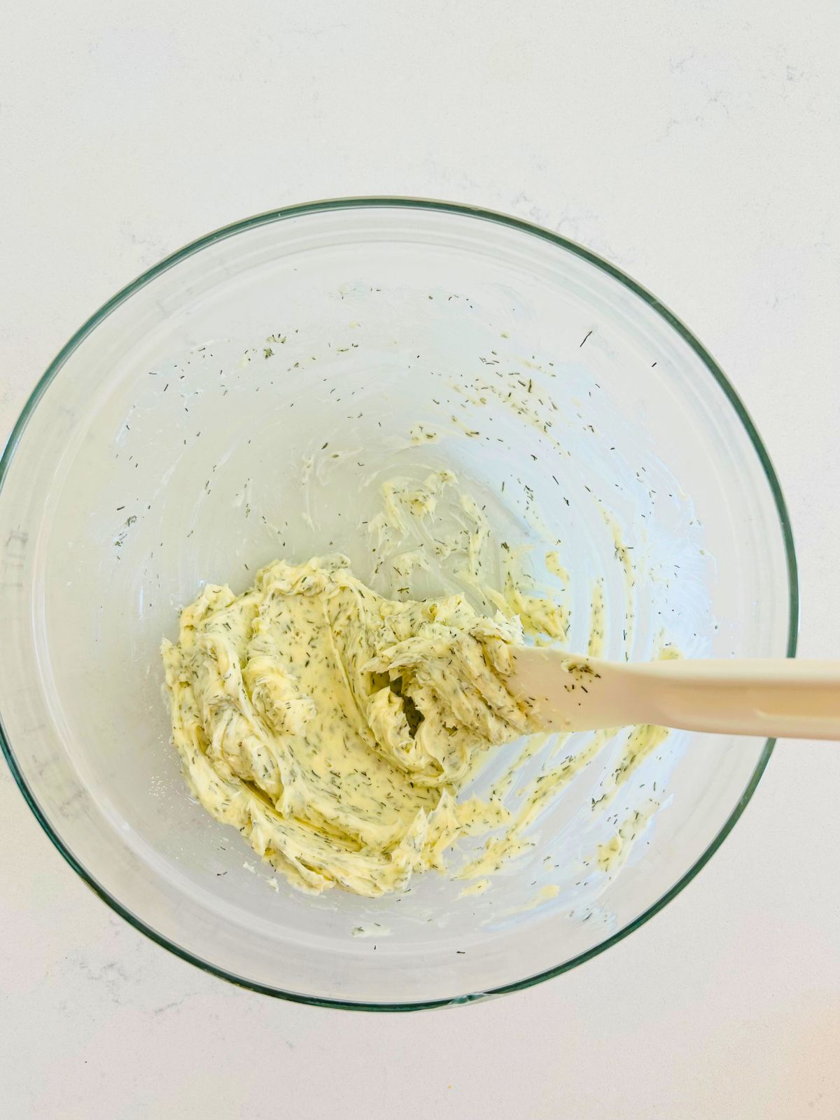 A clear bowl with butter, granulated garlic, and dried dill that were mixed together with the spatula.