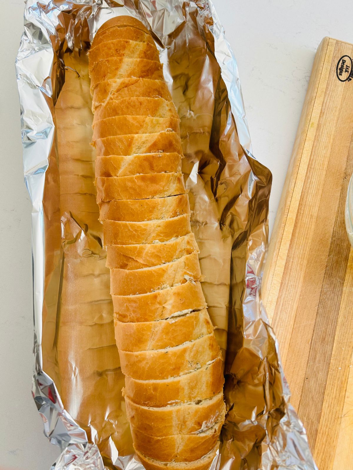 A sliced and buttered loaf of french bread laying on top of aluminum foil.