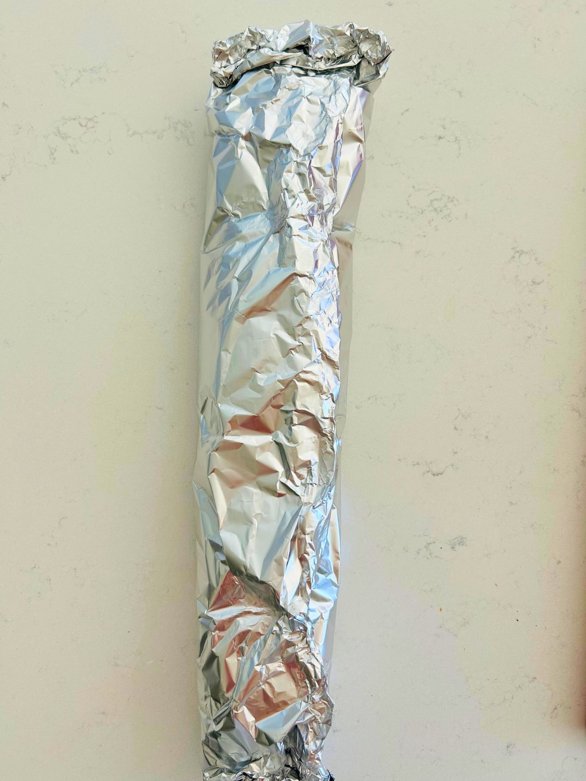 Aluminum foil wrapped around a loaf of garlic french bread ready for the oven.