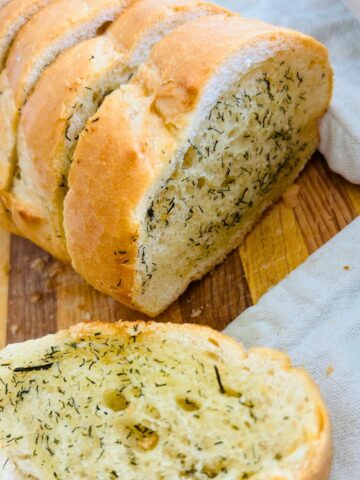 Thick sliced French bread with melted butter, granulated garlic, and dill weed on a cutting board.