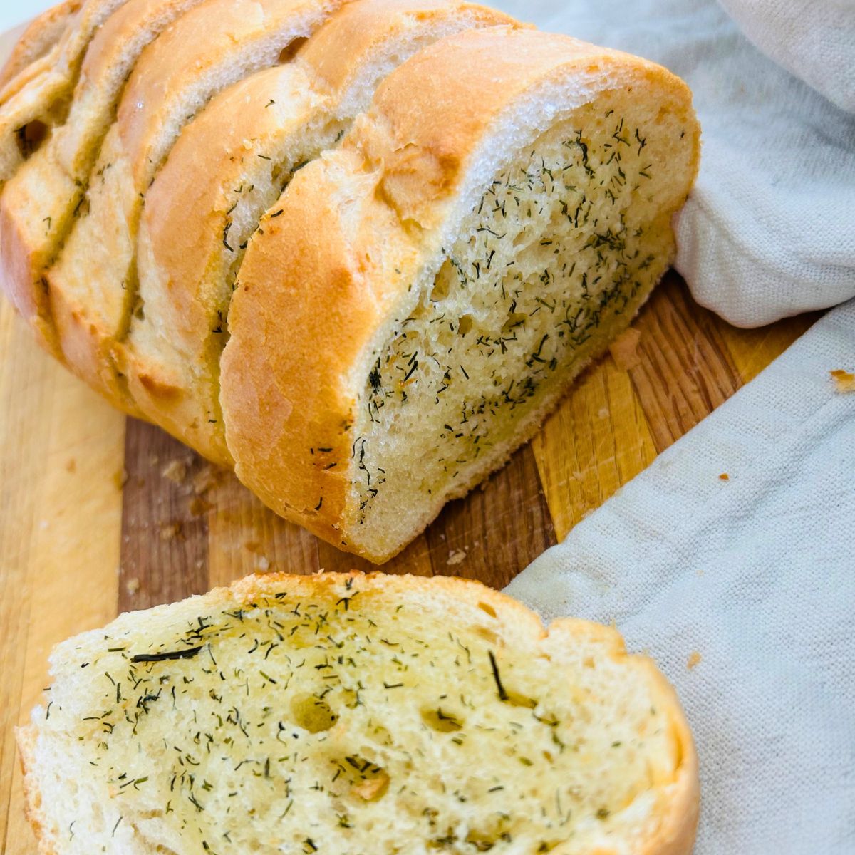 Thick sliced French bread with melted butter, granulated garlic, and dill weed on a cutting board.