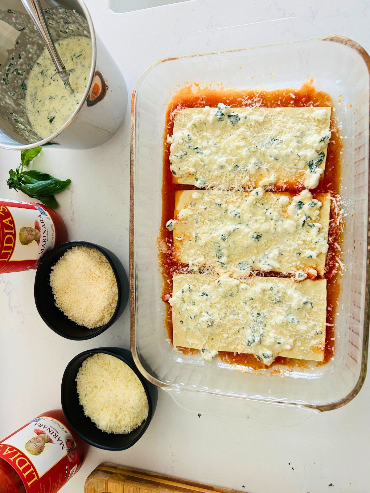 The first layer of making lasagna including marinara sauce, three no boil lasagna noodles, cottage cheese mixture, and grated Italian cheeses.