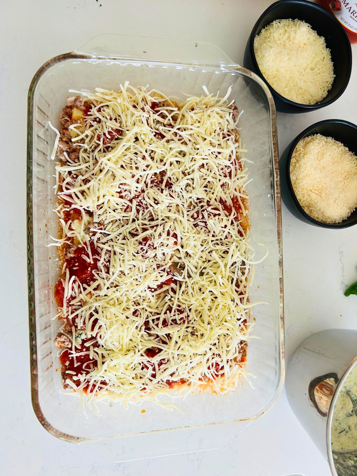 The first layer of making lasagna in a pyrex is complete with the spreading of shredded mozzarella cheese on top.