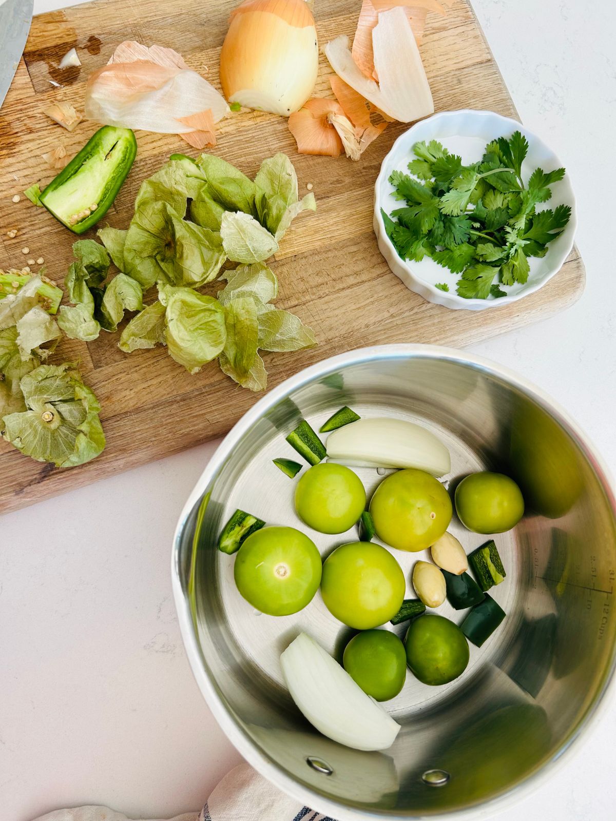 Peeled tomatillos, onion quarter, jalapeno pieces, and whole, peeled garlic in a saucepan.