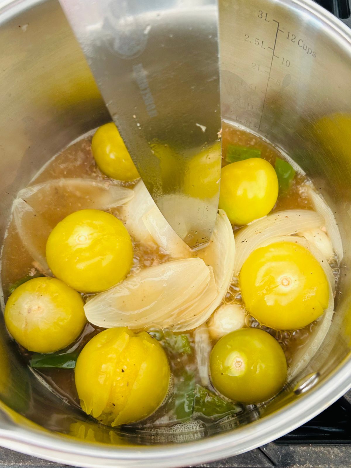 A saucepan of cooked tomatillos and jalapenos with a knife inserted into an onion.