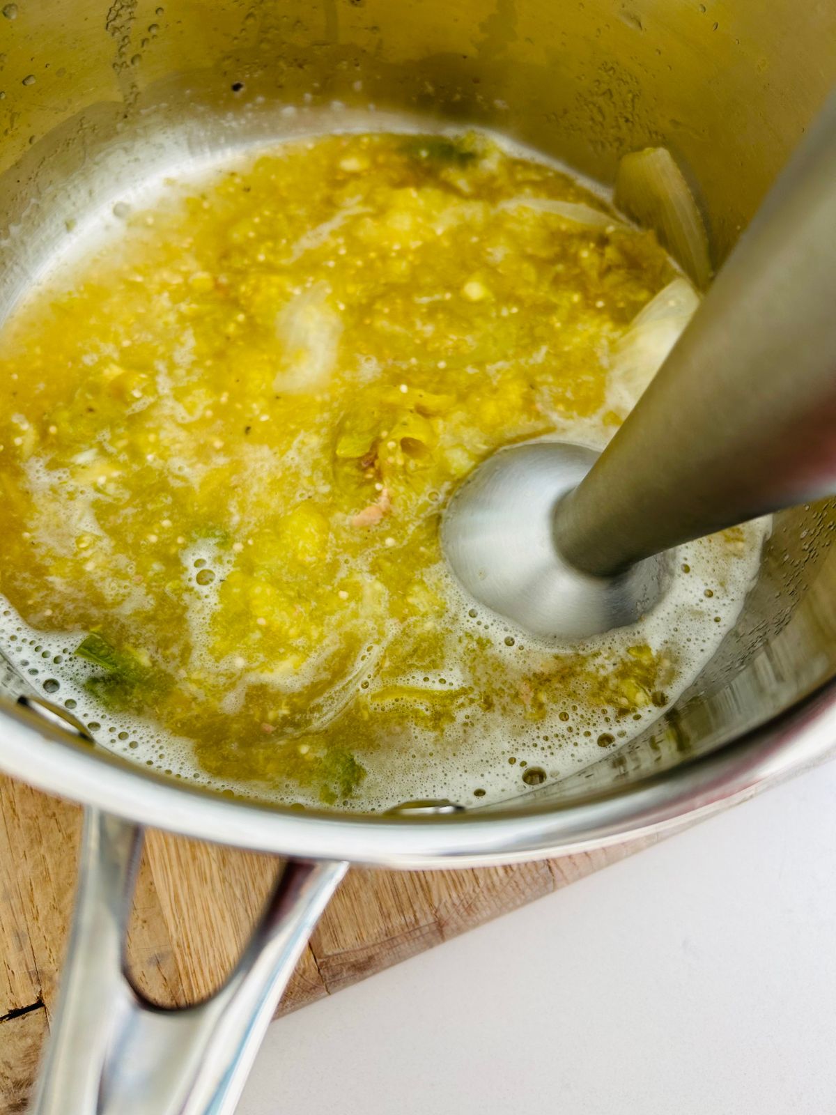 A stick blender is pureeing the tomatillos green salsa verde within the saucepan.