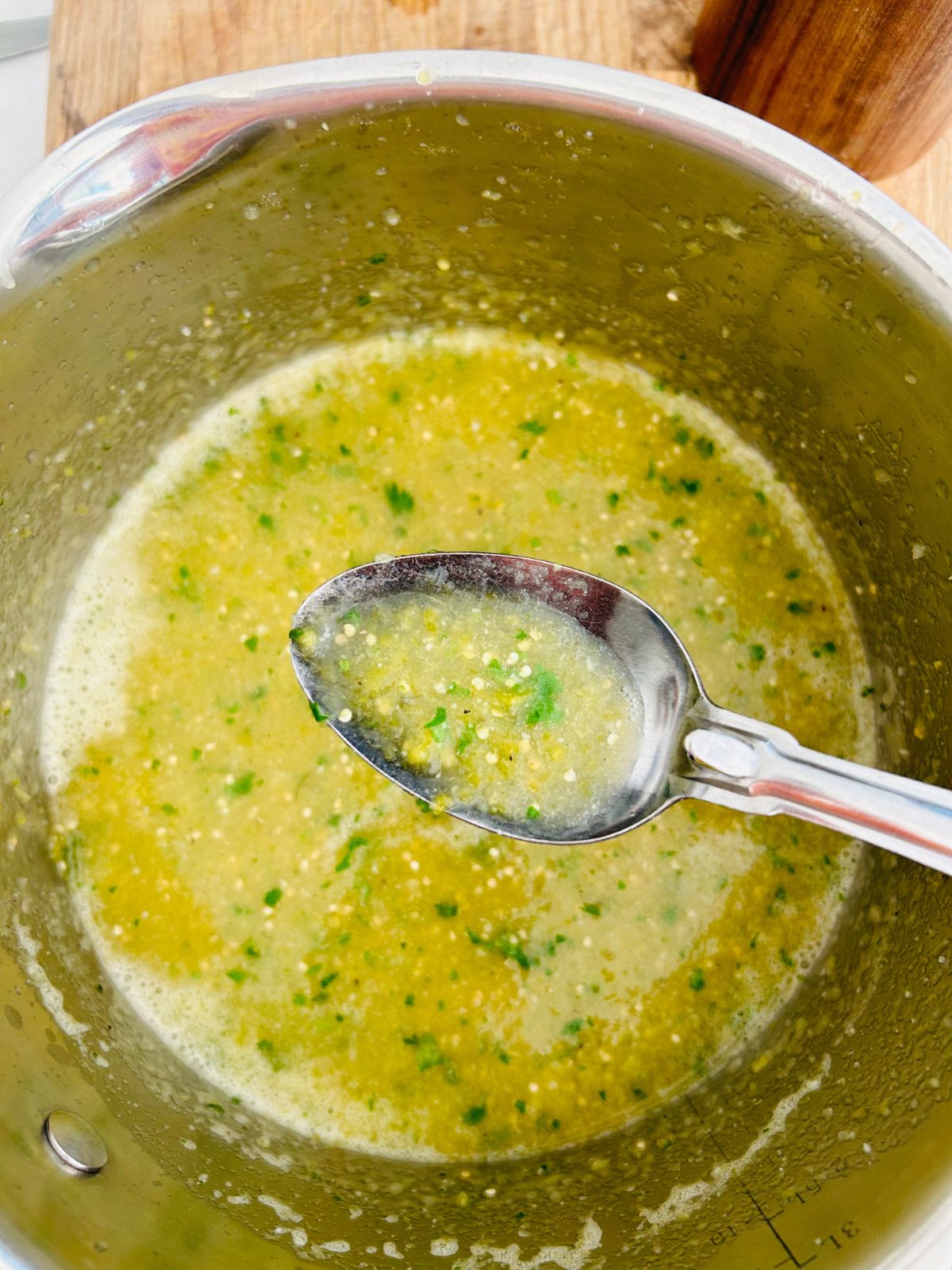 A spoon of the tomatillo green chili salsa over the pot after the cilantro has been blended into the salsa verde.