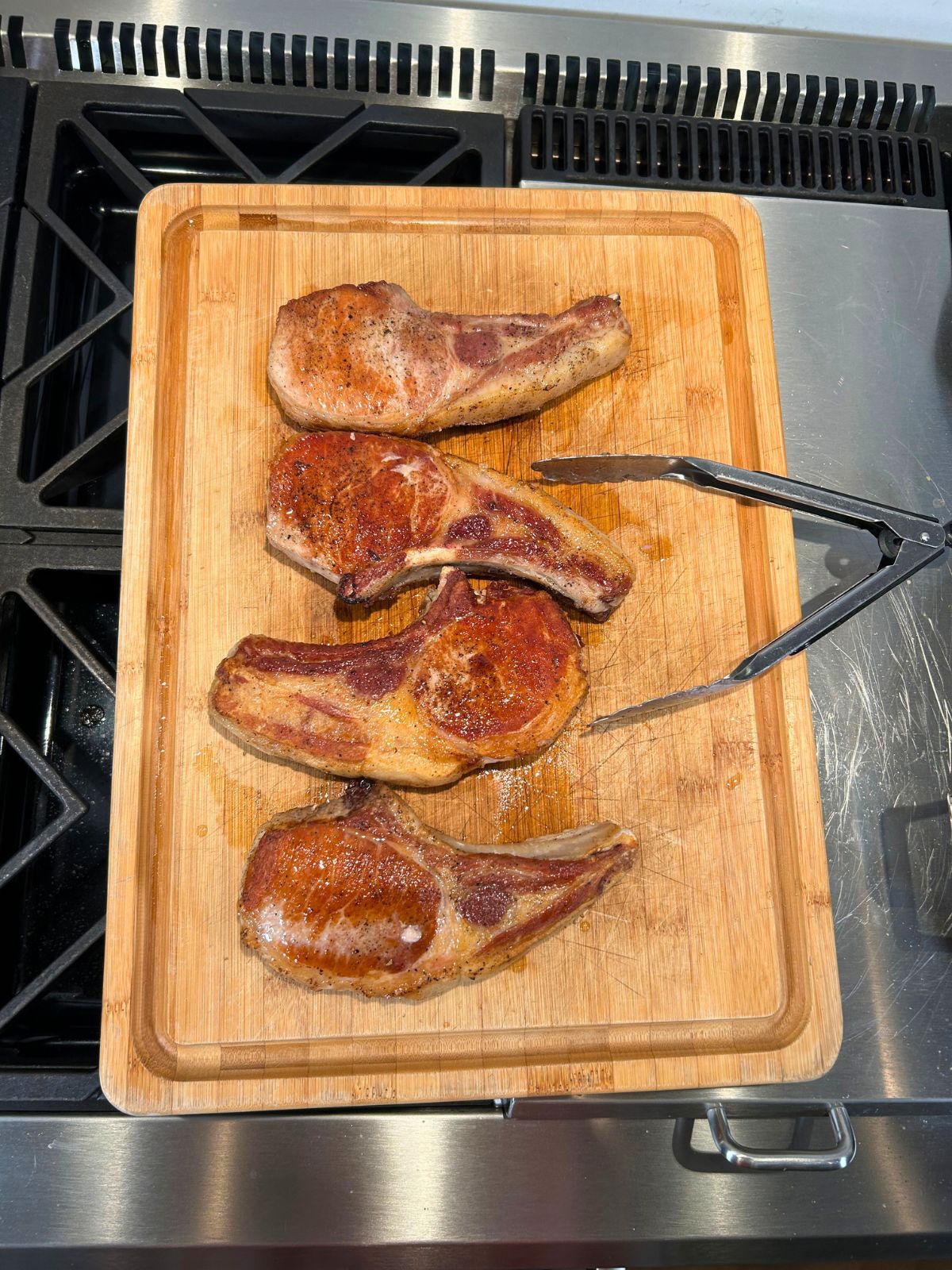 Seared pork chops and tongs resting on a cutting board.