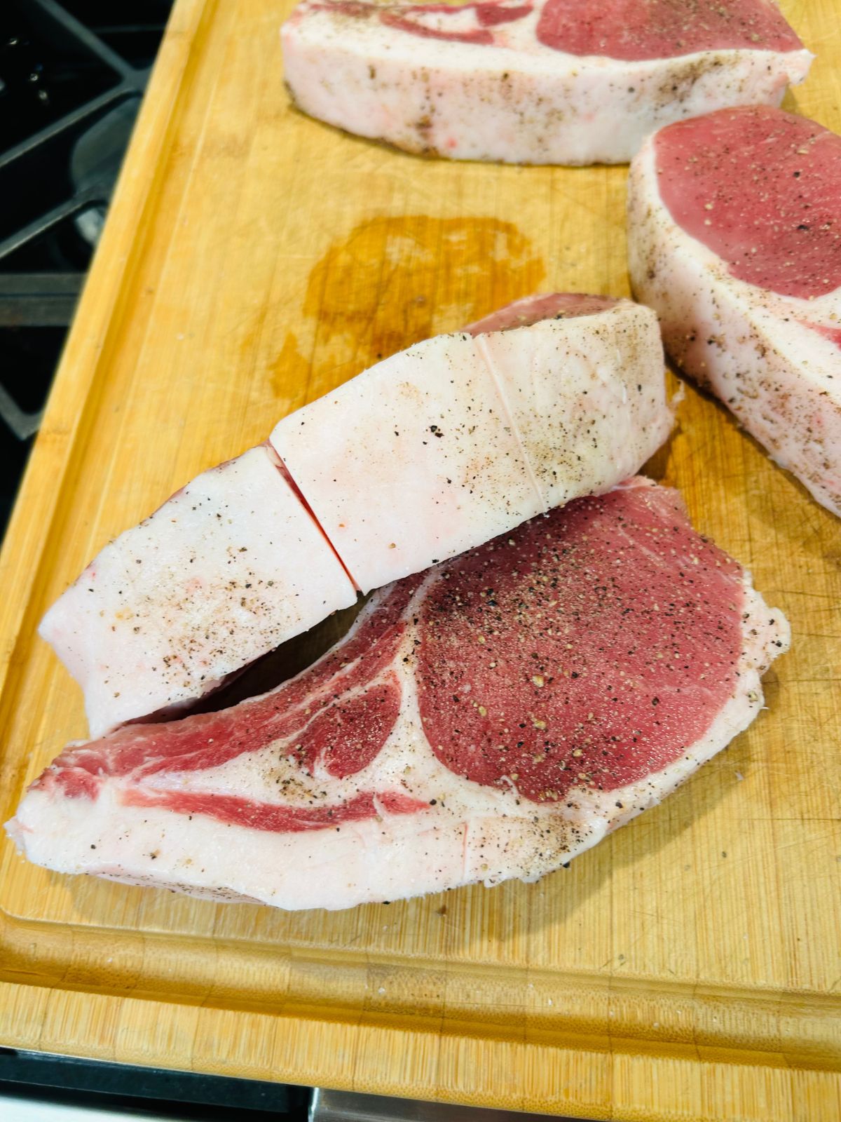 Pork chops are seasoned with their fat scored on the cutting board.