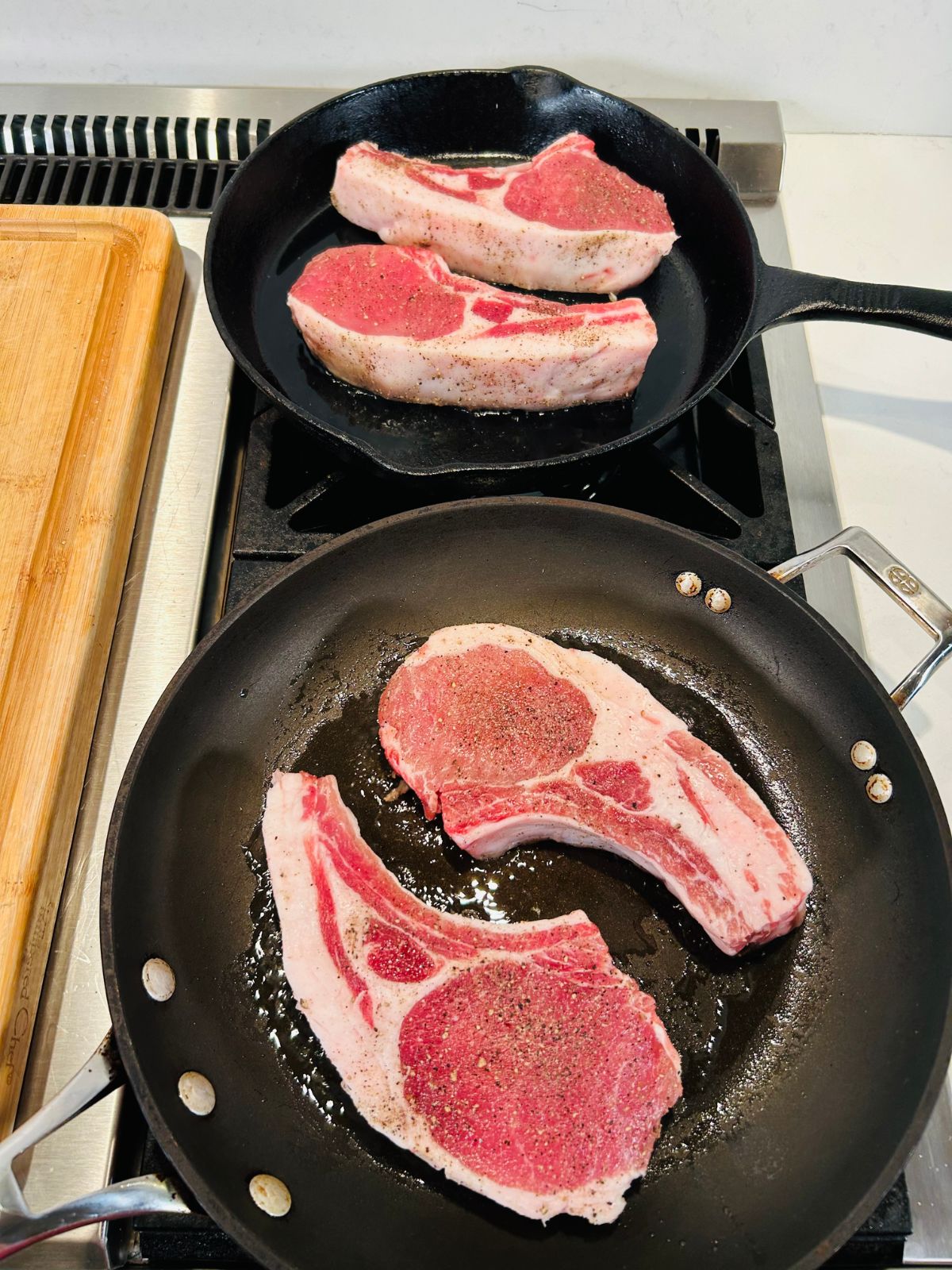 Starting the searing process of four thick pork chops in two different pans.