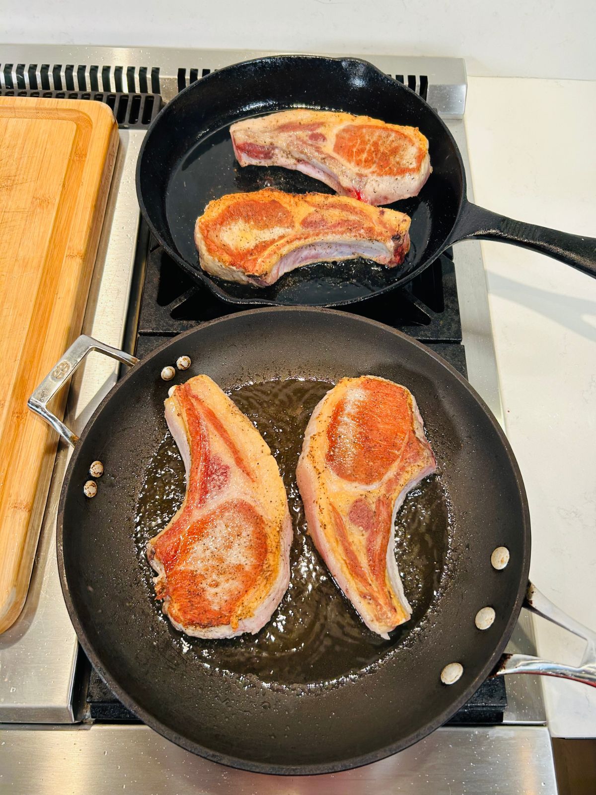 Two skillets holding two pork chops each searing the second side of the chops.