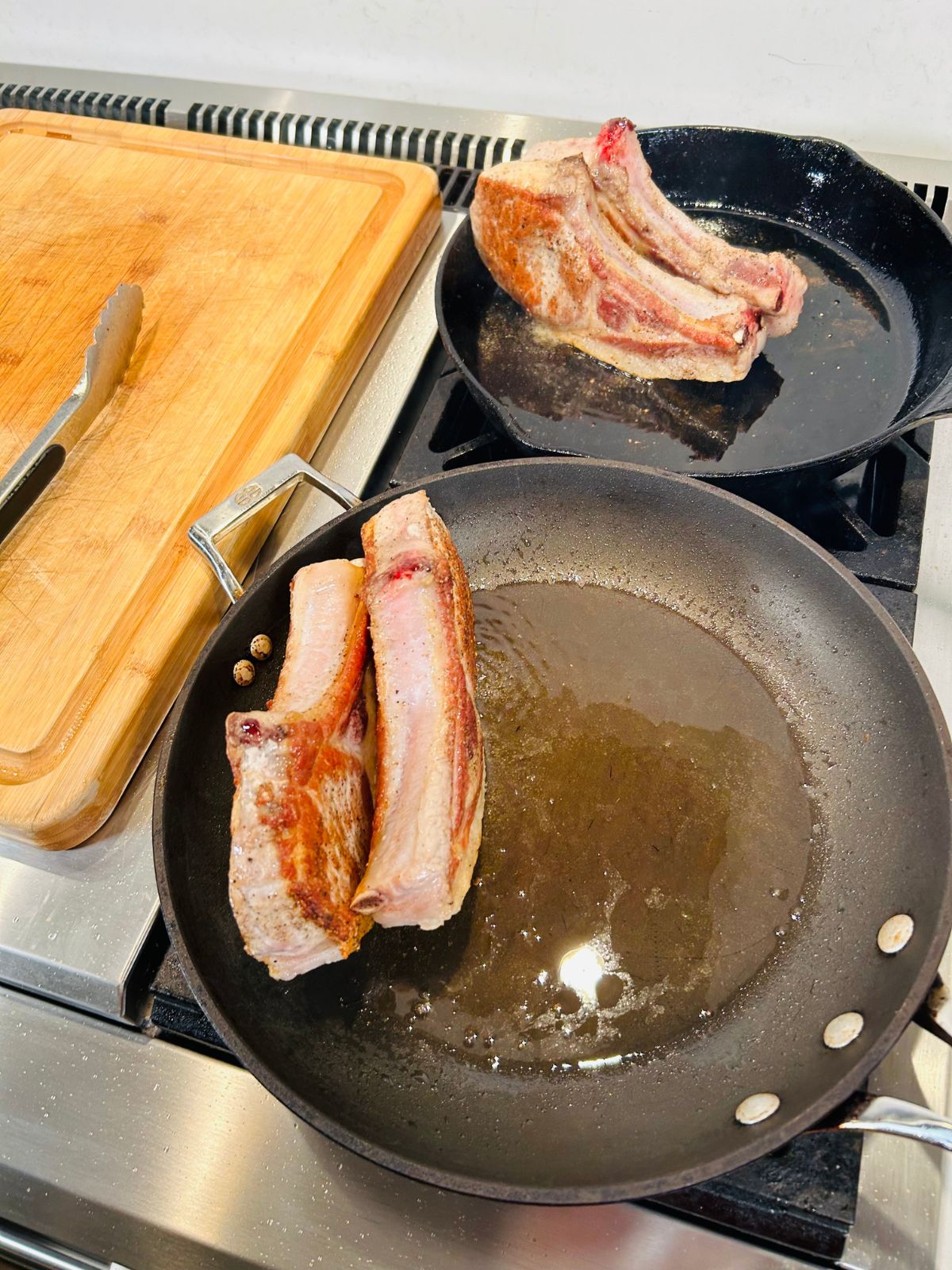 Two skillets searing the fat back side of pork chops.