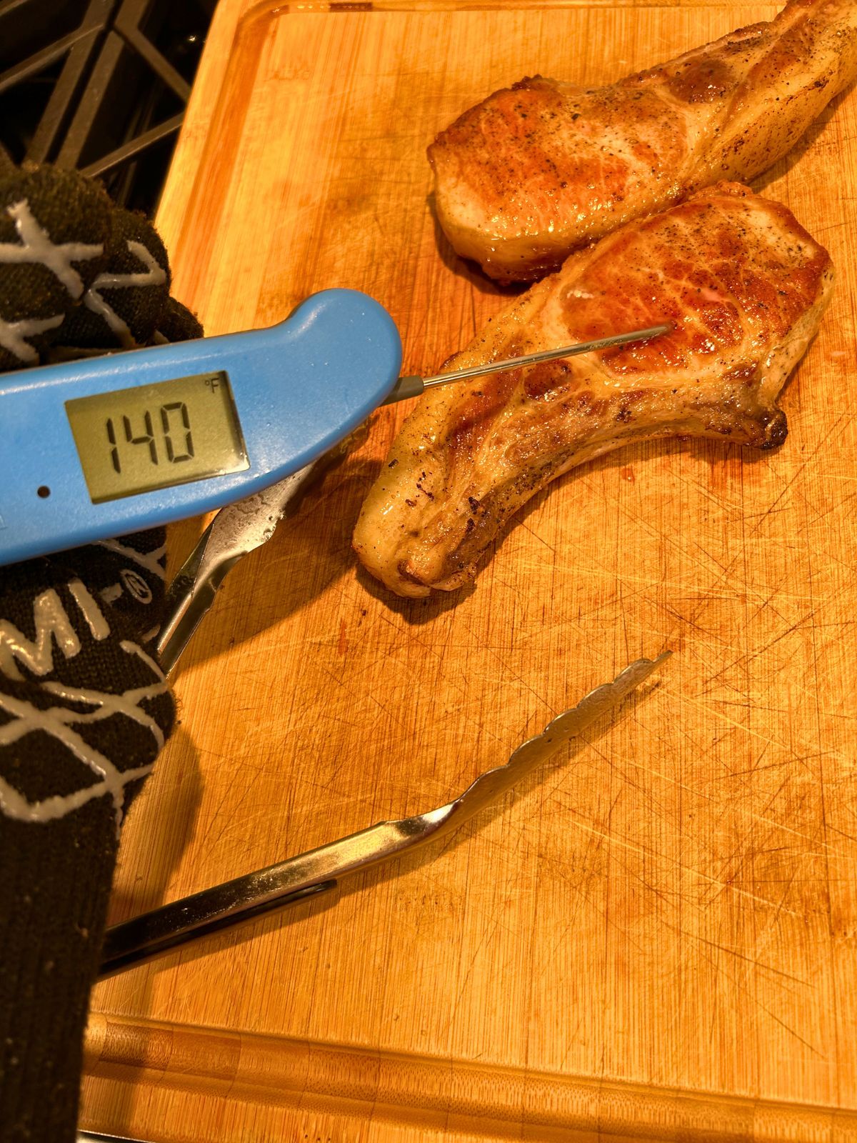 Pan seared thick pork chops resting on a cutting board with a temperature probe checking the internal temperature.