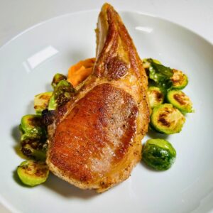 Pan seared pork chop resting on top of brussel sprouts and sweet potato puree.