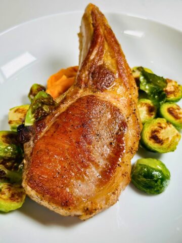 Pan seared pork chop resting on top of brussel sprouts and sweet potato puree.