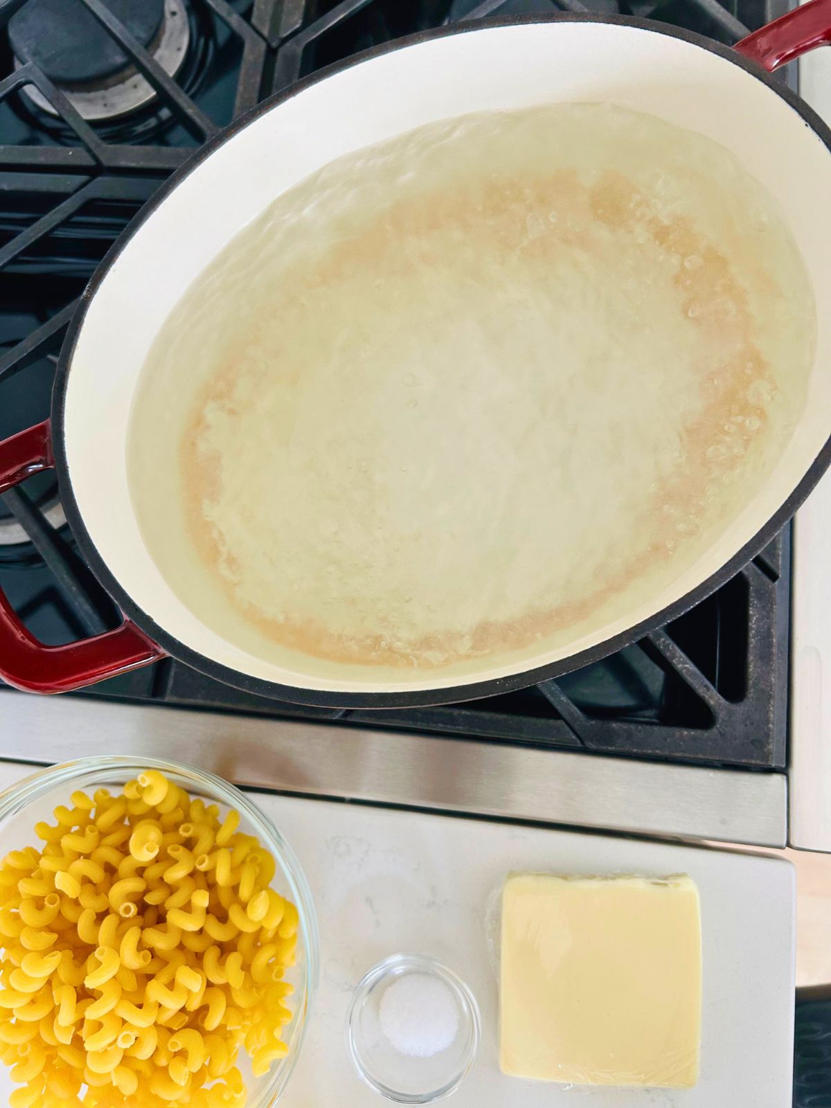 A pot of boiling water with dried pasta, salt, and American cheese next to it.