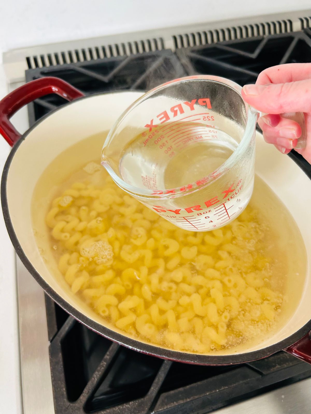 A pyrex filled with pasta water held over the pot of cooking pasta before draining it.