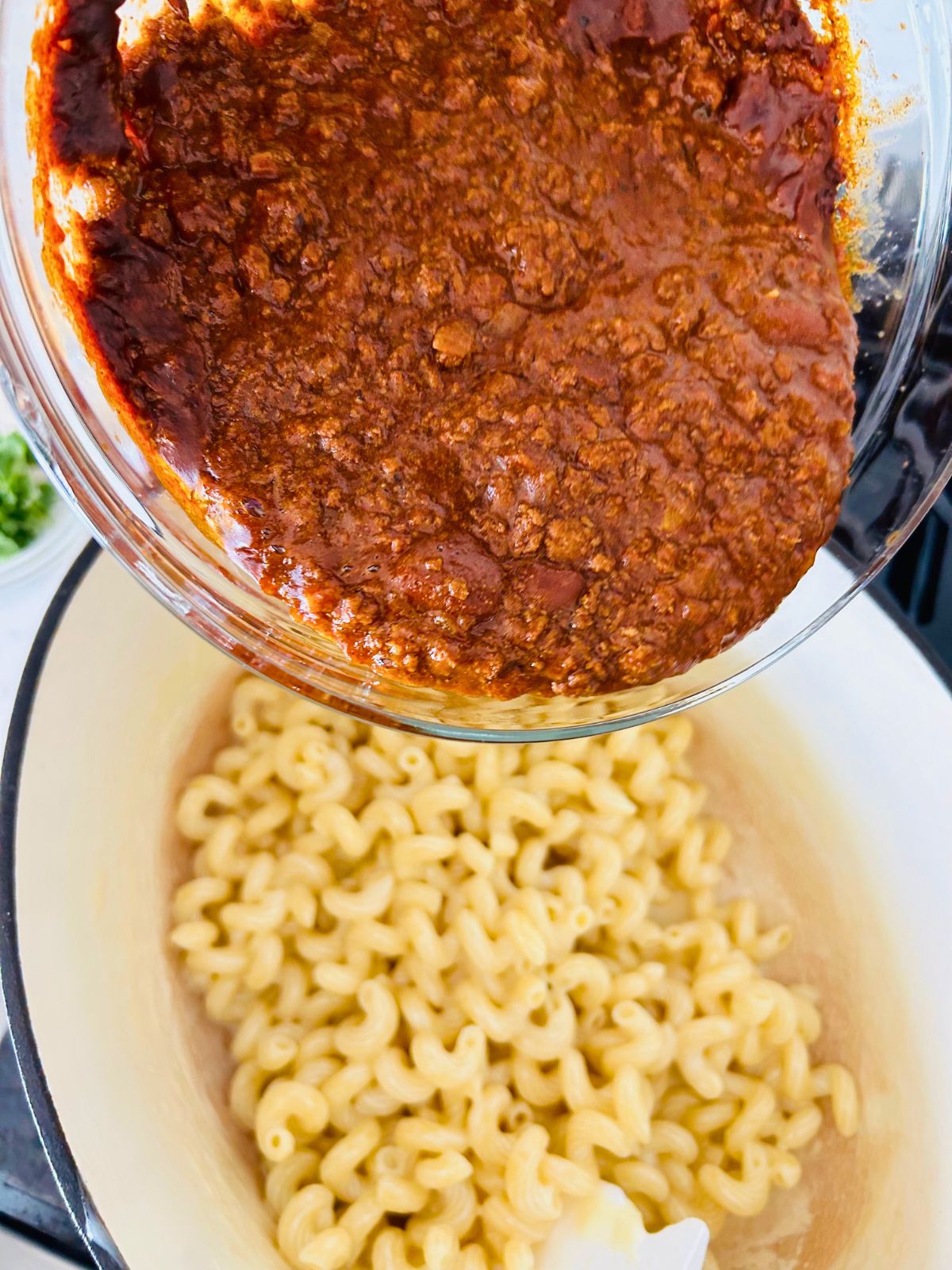 Warm, leftover chili in a clear bowl poured over the pot of macaroni and cheese.