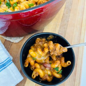 Chili mac with leftover chili in a black bowl with a spoon next to a napkin.