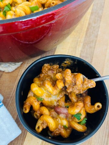 Chili mac with leftover chili in a black bowl with a spoon next to a napkin.