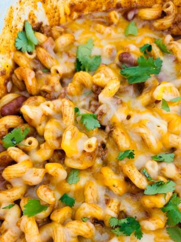 A pot of chili mac and cheese with melted cheese chopped cilantro on top.