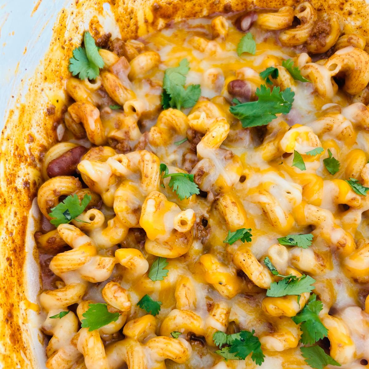 A pot of chili mac and cheese with melted cheese chopped cilantro on top.