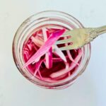 A fork holding a few quick pickled red onions above a mason jar.