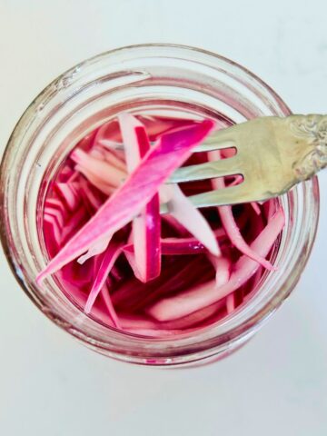 A fork holding a few quick pickled red onions above a mason jar.