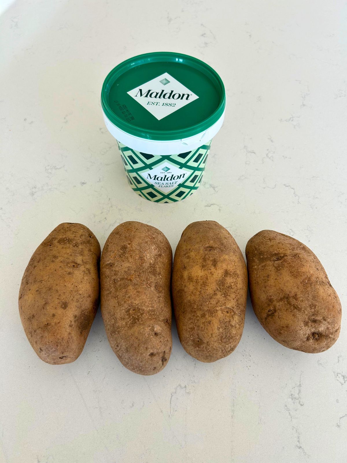 Russet baked potatoes and Maldon sea salt tub on the counter.