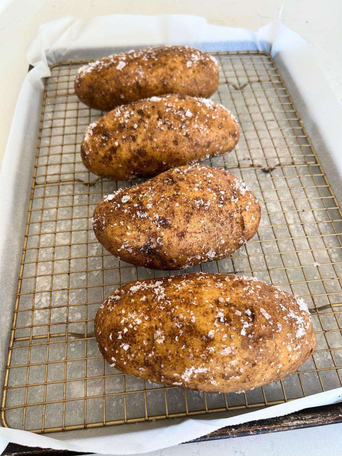 Four damp, salt crusted baked potatoes on a wire rack over a cookie sheet ready for the oven.