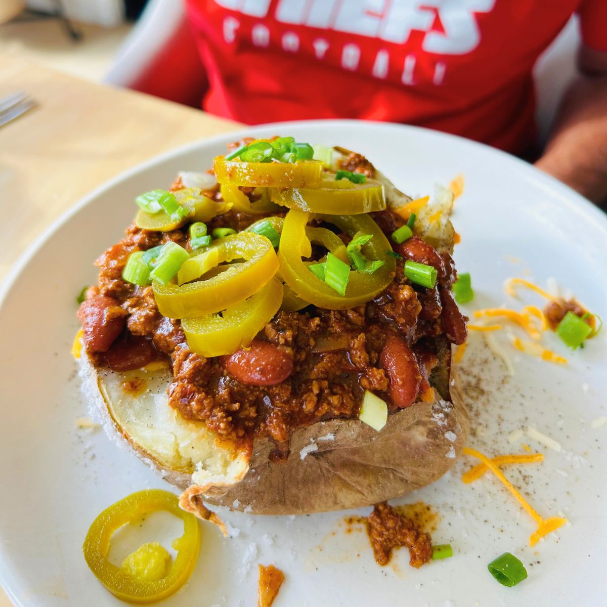 A baked potato split open with chili, cheese, green onions, and pickled jalapeños on top.