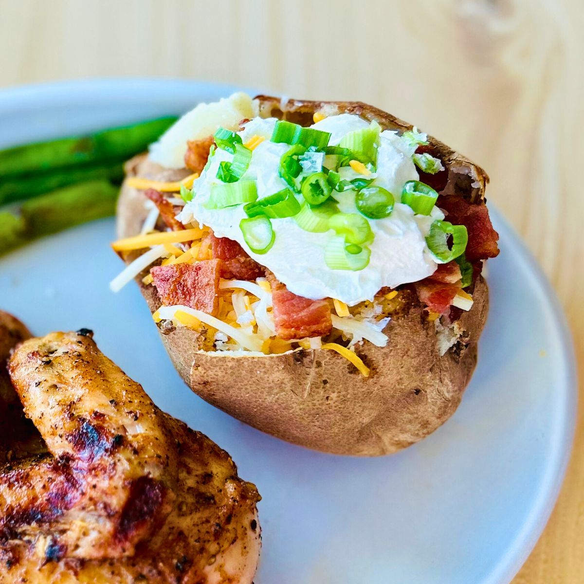 A loaded baked potato next to grilled chicken on a plate.