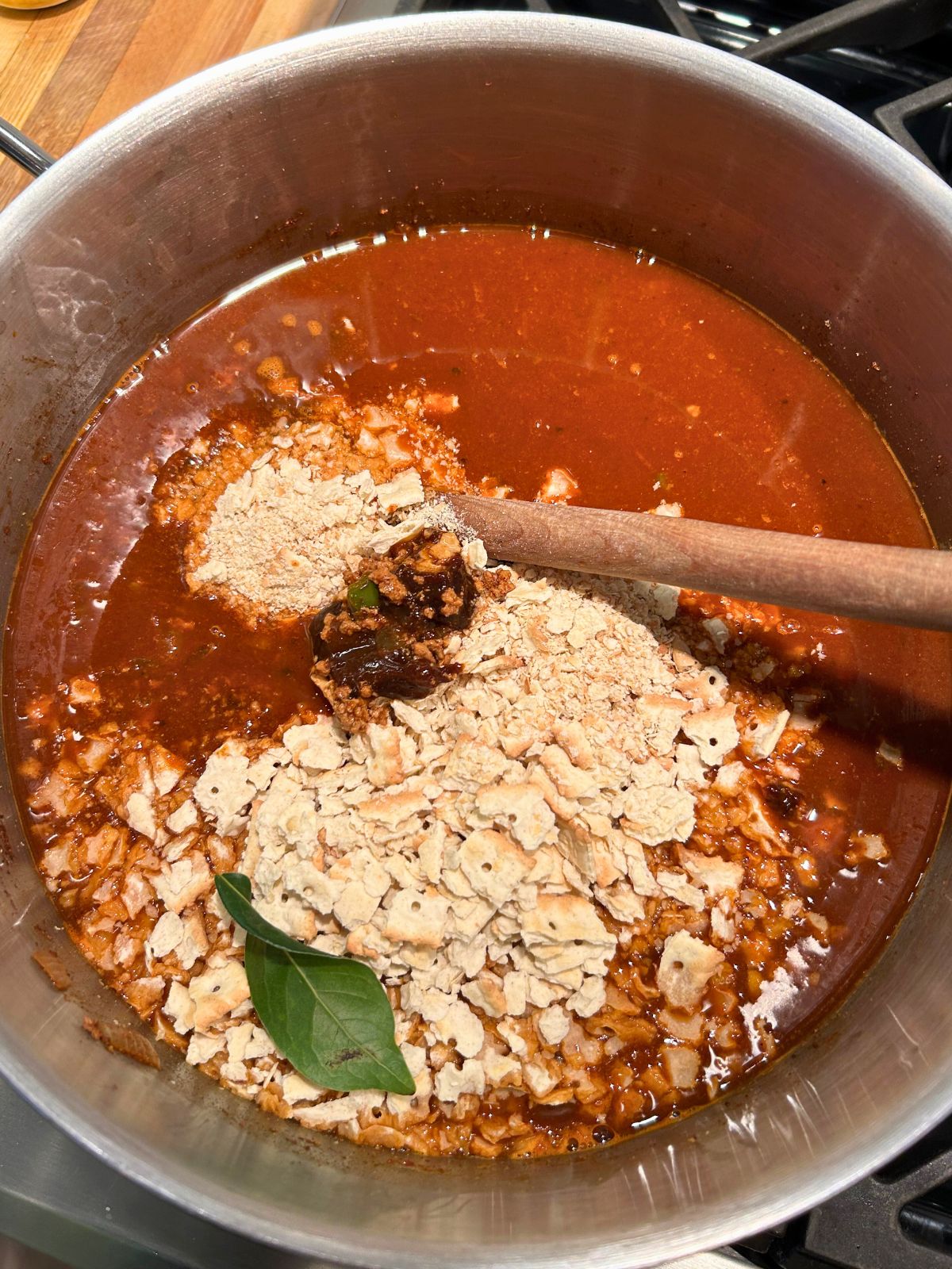 Crumbled saltines, veal demi-glace, and bay leaf added to a pot of chili over the stove.