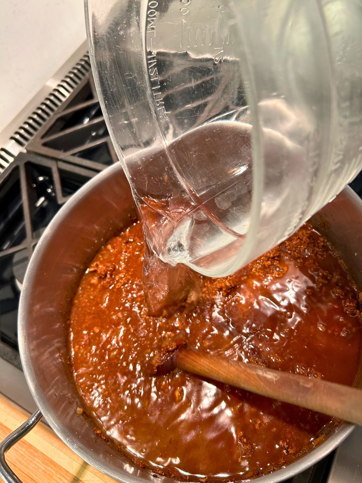 Six cups of water being poured into the pot of thick homemade chili.