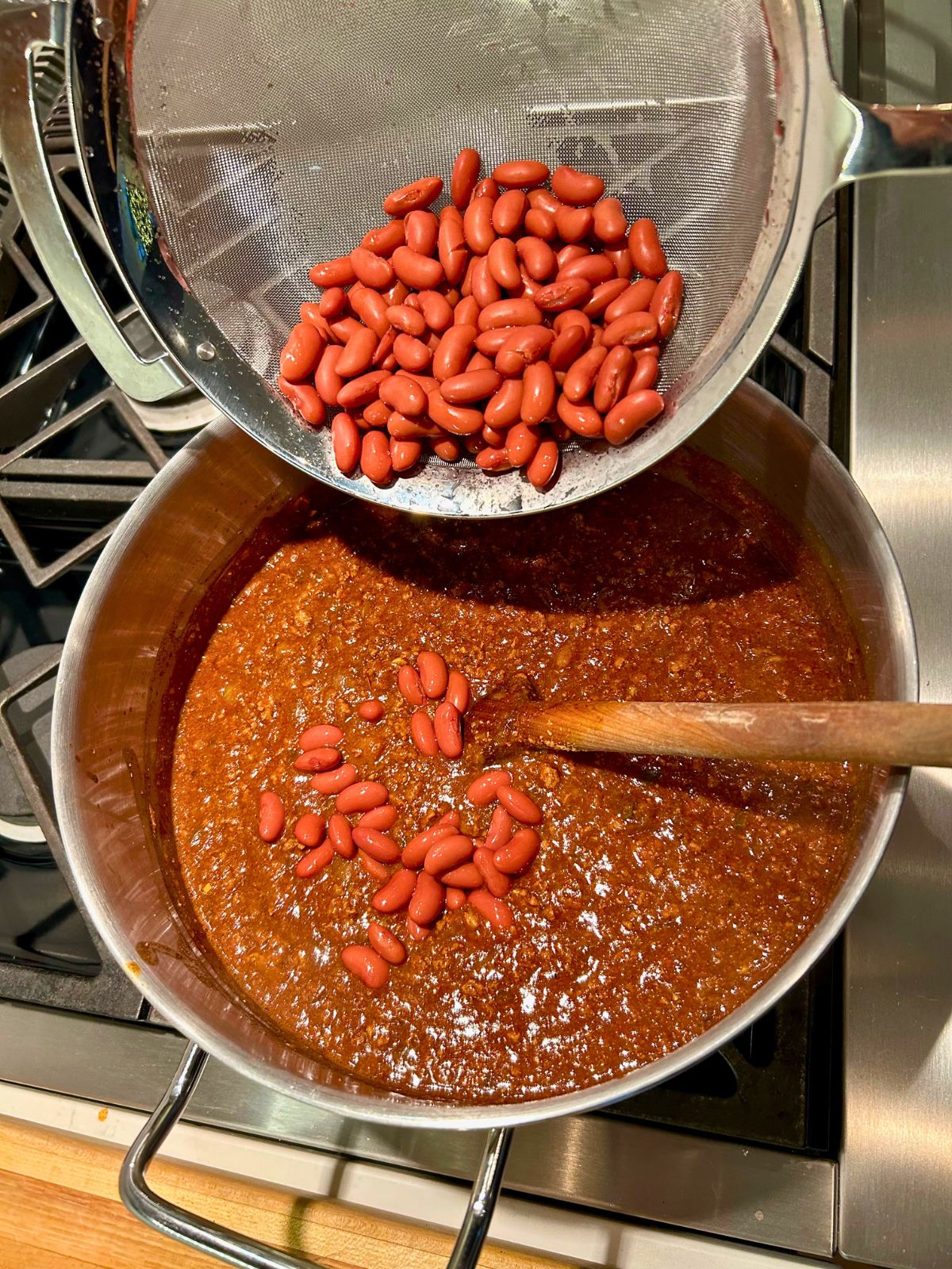 A can of rinsed red kidney beans in a colander going into the pot of chili.