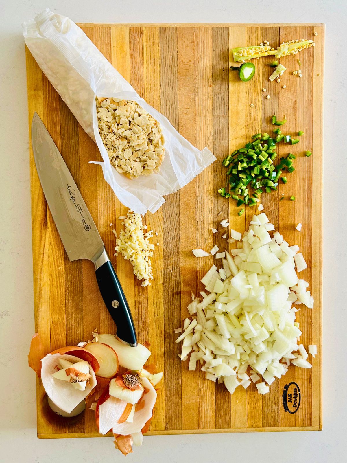 Chopped onion, chopped seedless jalapeno, minced garlic, and crumbled saltine crackers in their sleeve on a cutting board.