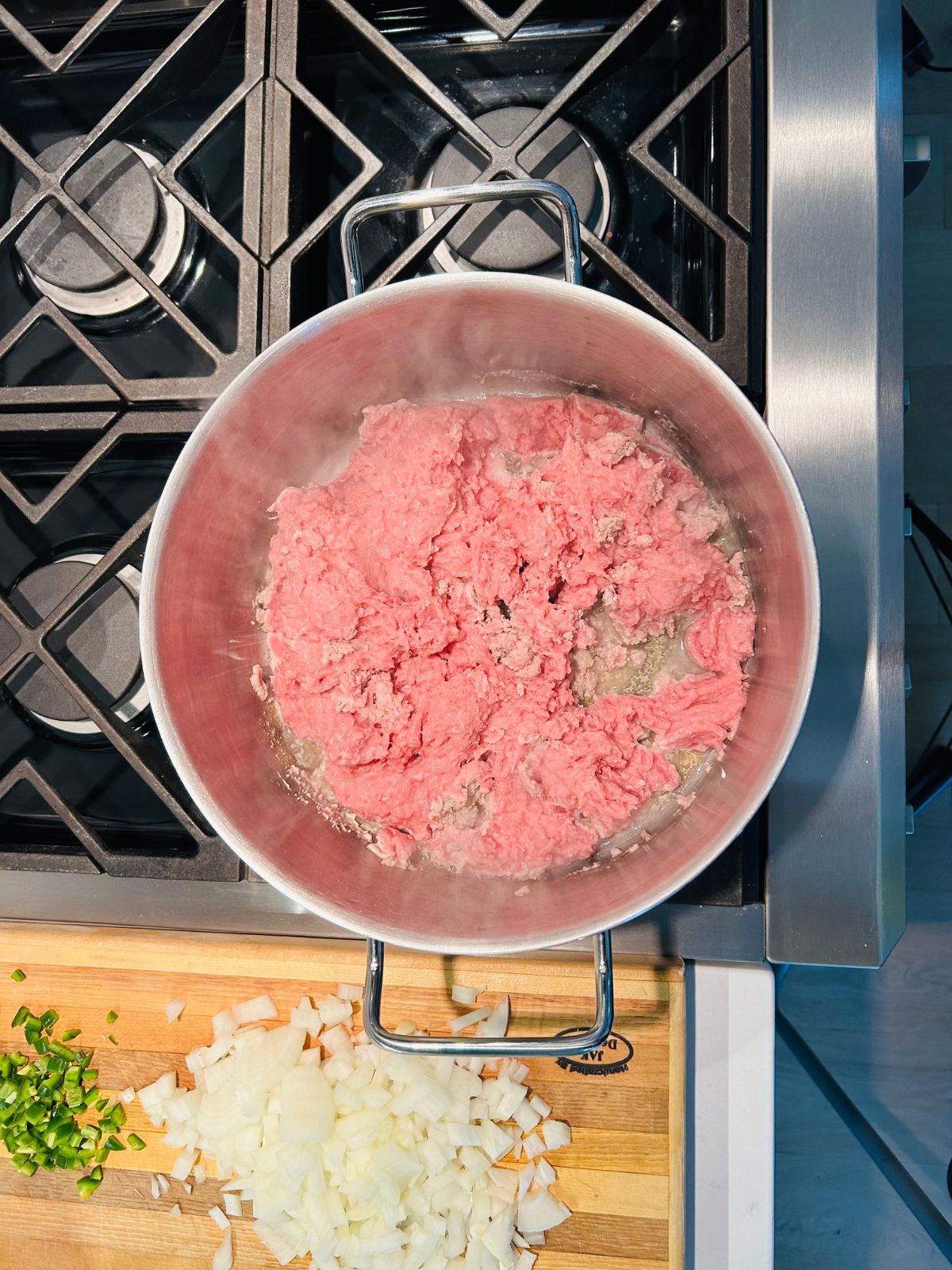 Ground turkey browning in a pot next to a cutting board holding chopped onions and jalapenos.