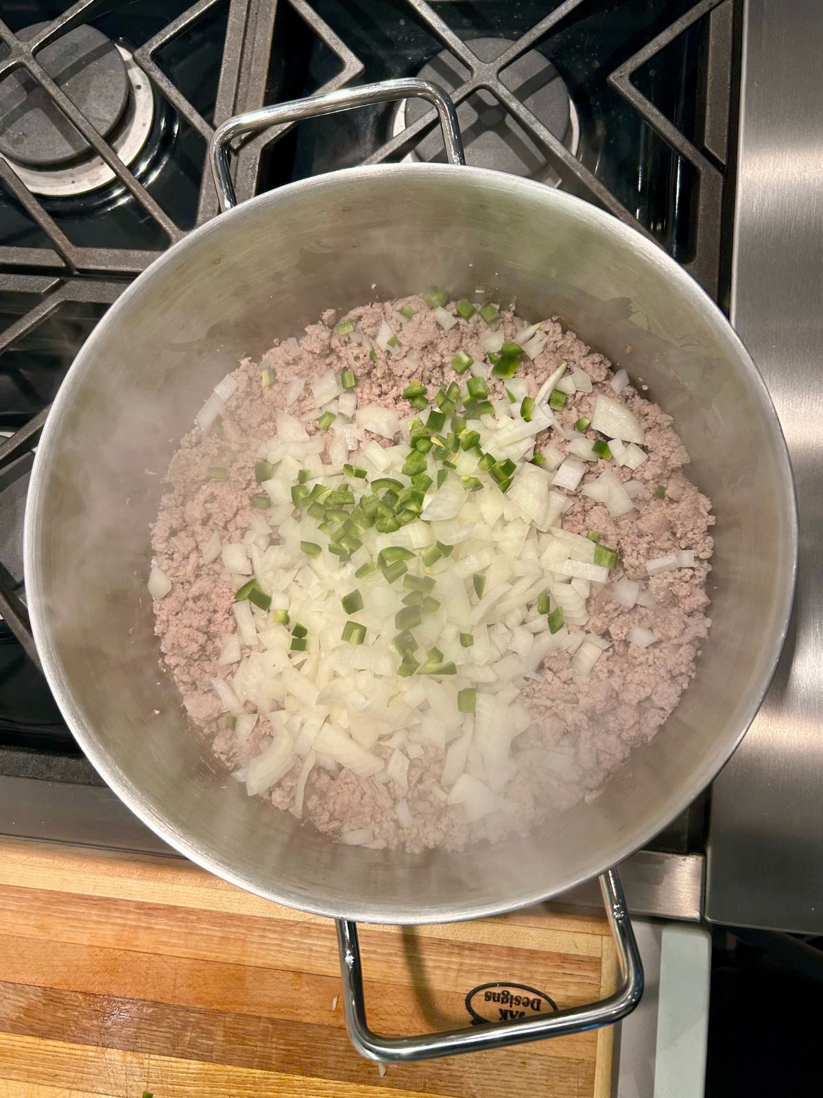 A pot of cooked crumbled ground meat with raw chopped onions and jalapeno on top.