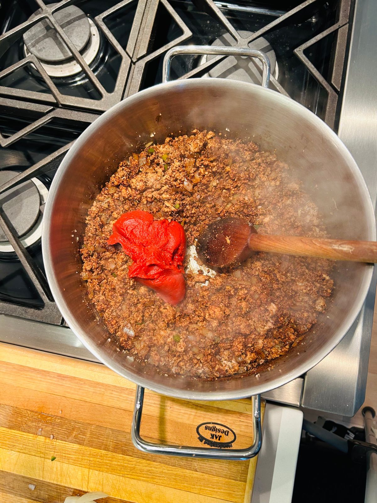 Tomato paste has been added to the pot of chili seasoned ground meat mix.